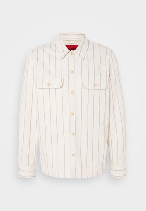 Bijela košulja-jakna s bež vertikalnim prugama, dva džepa na prsima i gumbima za zatvaranje. Ima klasični ovratnik i manžete na rukavima.