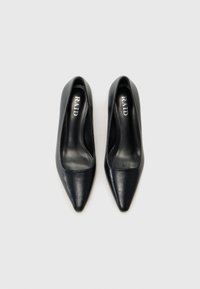 Bombas de tacón alto de cuero negro con diseño de punta afilada. Textura suave y estilo minimalista, con una plantilla de marca.
