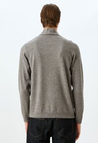 Grå, långärmad tröja med texturerad stickning, platt krage och ribbad nederkant. Bärs med mörka denimjeans som visar en kroppsnära design.