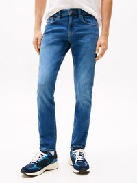 Blå denimjeans med slim fit, som har fem lommer, glidelås og knappelukking. Brukt med blå og svarte joggesko.