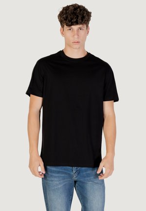 Camiseta de algodón negra con cuello redondo y mangas cortas, llevada por un modelo con jeans de mezclilla claros, diseño sencillo, sin logotipos ni patrones visibles.