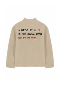 Giacca in pile beige con testo nero e rosso sul retro che recita: "Un po' di ♥ in questo mondo brutale (ma non troppo)."