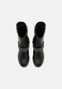 Botas de cuero negras hasta el tobillo con suela plana, que presentan un grueso acento de cadena plateada en el empeine y hebillas en los laterales como detalle.
