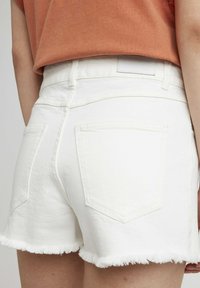 Shorts en denim blanc avec un ourlet effiloché, deux poches arrière et une texture lisse, agrémentés d'une taille ajustée.