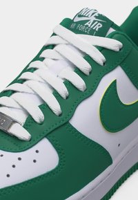 Εγγύς λήψη πράσινου και άσπρου παπουτσιού Nike Air Force 1 με λευκά κορδόνια και πράσινο λογότυπο swoosh με κίτρινη περίγραμμα.