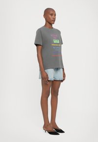 Grå kortermet t-skjorte med fargerike tekstlogoer, kombinert med denimshorts og svarte hælede mules. En enkel, tettsittende design.