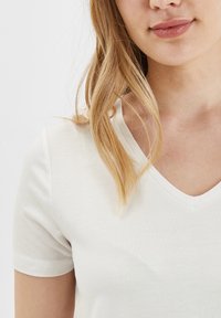 T-shirt bianca a scollo a V con maniche corte, realizzata in tessuto morbido. Il colletto è bordato e veste aderente, con una leggera elasticità.