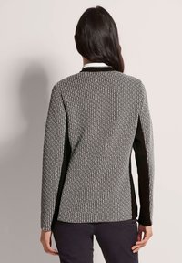 Langärmliger Pullover mit schwarz-weißem Muster und strukturiertem Strickdesign, mit schwarzen Seitenpaneelen und einem subtilen Kragen-Detail.