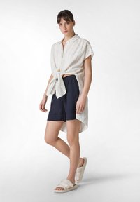 Lettet, stribet linned skjorte med en frontknude, matchet med marineblå shorts og neutrale slidesandaler, med en afslappet pasform og blød tekstur.