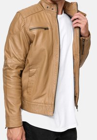 Hellebraune Lederjacke mit gesteppter Schulterpartie, hohem Kragen, Reißverschluss vorne und Seitentaschen, getragen über einem weißen Hemd.