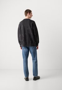 Sudadera negra con un corte relajado, patrón texturizado y puños de canalé, combinada con jeans de color azul claro y zapatos negros.