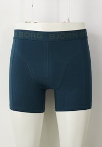 Férfi turkiz színű boxer alsónemű, sima anyagból készült, zöld logós derékpánttal és illeszkedő szabással, varrott élekkel.