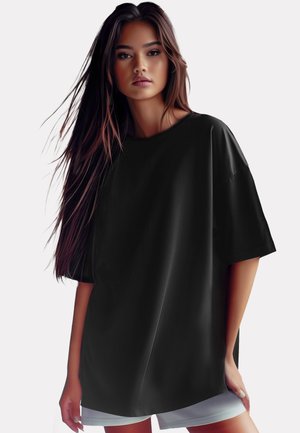 Schwarzes, übergroßes T-Shirt mit kurzen Ärmeln, Rundhalsausschnitt, sanfter Textur und lässiger Silhouette. Getragen mit hellen Shorts.