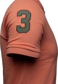 Kortärmad, korallfärgad polotröja med en strukturerad tyg och ett grönt broderat nummer "3" på vänster ärm.