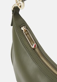 Coin d'un sac à main en cuir vert olive avec fermeture éclair dorée et tirette ronde arborant des rayures rouge, blanc et bleu.
