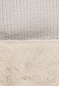 Berretto lavorato a maglia con la parte superiore di un grigio chiaro testurizzato e la parte inferiore di un beige morbido e peloso, uniti da una cucitura precisa.