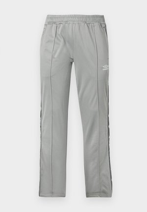 Lyse grå Umbro sportbukser med elastisk midjebånd og svart-hvite sidestropper, vist mot en hvit bakgrunn.