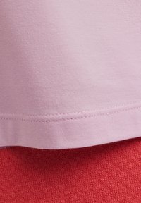 Tessuto di cotone rosa chiaro con una texture liscia, caratterizzato da un orlo con cuciture diritte, sovrapposto a un tessuto lavorato a maglia rosso.