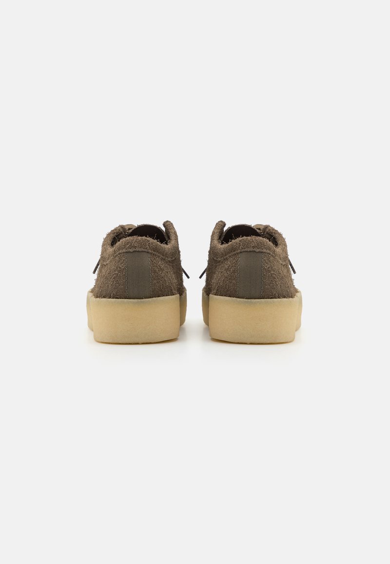 Une paire de chaussures brunes à texture duveteuse avec des semelles épaisses beiges, vues de l'arrière sur un fond blanc.
