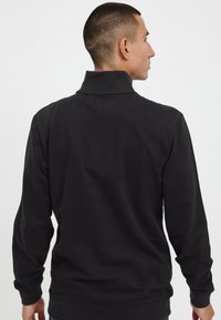 Black pullover sweatshirt with a high collar, long sleeves, and ribbed cuffs, made from a soft, thick cotton material.