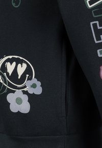 Schwarzer Stoff mit einem Druckmotiv, das zwei Lavendelpflanzen und ein weißes Smiley-Gesicht mit herzförmigen Augen zeigt.