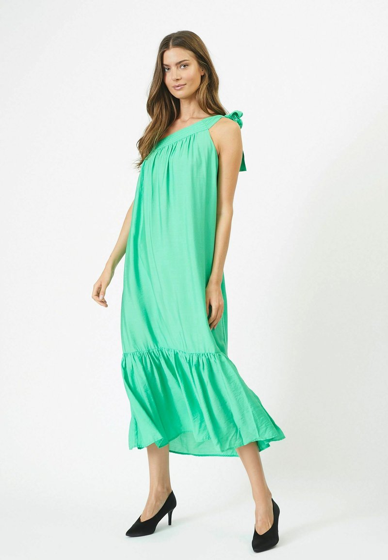 Rochie maxi verde, fluidă, cu tiv în straturi, decolteu gathered și detalii cu fundiță pe umăr. Textură netedă și material ușor.