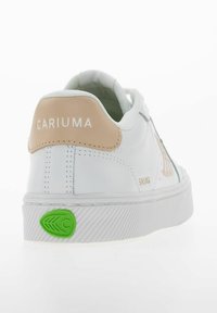 Białe sneakersy z beżowym elemencie na pięcie, zielonym akcentem na podeszwie, teksturowaną gumową podeszwą i haftowanym logo. Gładki materiał syntetyczny z subtelnymi detalami.