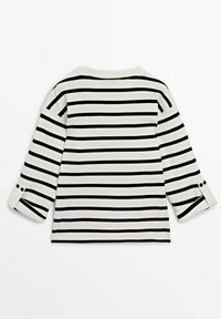 Chemise blanche à manches longues avec des rayures noires horizontales, dotée de poignets boutonnés et d'une texture côtelée, posée à plat montrant le dos.