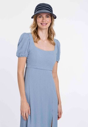 Šviesiai mėlyna suknelė su tekstūrizuota medžiaga, pūstomis rankovėmis ir kvadratiniu iškirpimu, su šoniniu plyšiu. Derinama su tamsiai mėlynu raštuotu skrybėle.