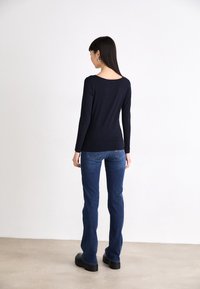 Marineblauw shirt met lange mouwen en een ronde hals, gecombineerd met donkerblauwe flared jeans en chunky zwarte platform schoenen, met details op de achterzakken.