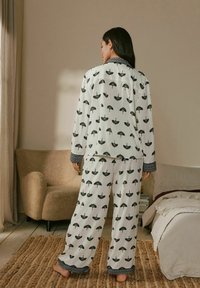 Weißes Pyjama-Set mit schwarzen Regenschirmmustern, langärmligem Oberteil mit gemusterten Bündchen und weit geschnittenen Hosen. Weiche, strukturierte Stoffqualität.