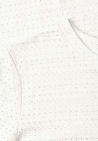 Hvid tekstureret strikstof med mønster af små hævede prikker og horisontale striber, der viser halsudskæring og skuldersømme.