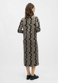 Ilga, raštuota suknele smėlio spalvos su juodais bangų raštais. Turi tiesią siluetą ir ilgas rankoves. Dėvima su juodais batais.