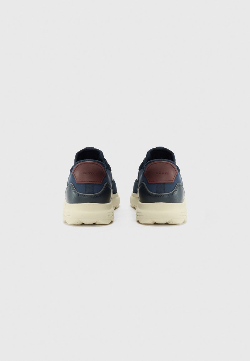 Zapatillas de deporte azul marino con parte superior de cuero texturizado, acentos burdeos contrastantes y suela color crema. Talón redondeado y diseño sin cordones.