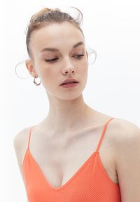 Top arancione a coste con spalline sottili e scollatura a V. Presenta un tessuto liscio e una sottile texture, mettendo in risalto l'area del collo e delle spalle.