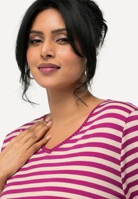 Camiseta de algodón con escote en V, con rayas verticales en rosa y blanco y detalles metálicos decorativos a lo largo del escote.