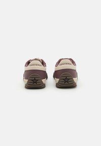 Ténis Converse castanhos e beiges, de cano baixo, com um detalhe de estrela no calcanhar e sola de borracha texturizada para melhor aderência.