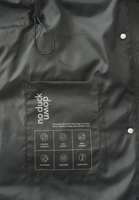 Schwarze Jacke mit einem Recycling-Insulation-Tag, der Symbole für Atmungsaktivität, Wärme und Einstellbarkeit zeigt. Glatte, glänzende Oberfläche.