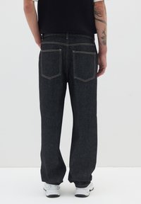 Jeans de mezclilla oscura con corte recto, bolsillos traseros visibles y costuras beige en contraste. Combinados con zapatillas blancas.