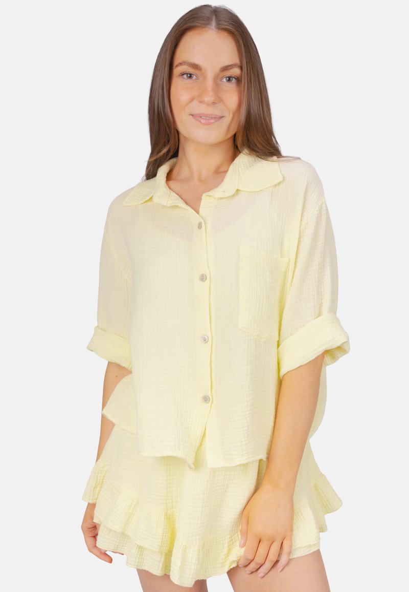 Ensemble jaune à deux pièces comprenant une chemise à boutons avec une poche et des manches retroussées, ainsi qu'une jupe à volants, fabriquée en coton texturé.