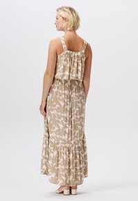 Beżowa sukienka maxi w białe wzory ptaków, z szerokimi ramiączkami, marszczonym stanikiem oraz falbaniastej spódnicy. Teksturowana tkanina, casualowy krój.