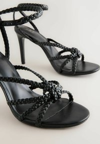 Schwarze High-Heels Sandalen mit geflochtenen Riemen, offener Zehenpartie und glattem Lederfinish. Verfügt über aufwendige geflochtene Details an der Vorderseite.