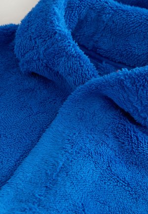 Mehekina, gosta modra flis tkanina z vidnimi šivi in delom ovratnika ali pregiba, ki prikazuje teksturo in prijeten material.