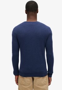 Maglione in lana blu navy con collo rotondo, maniche lunghe e polsini e bordo a costine. Texture liscia e design aderente, visto da dietro.