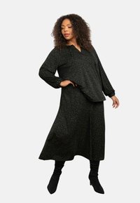 Abito midi a stampa leopardata nera con vestibilità ampia, maniche lunghe e scollatura a V. Abbinato a stivali neri alti fino al ginocchio. Tessuto morbido.