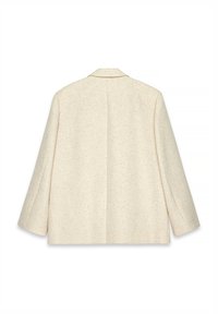 Blazer couleur crème en tissu texturé, avec un col cranté et une coupe ample. Il possède une fente à l'arrière et deux poches latérales.