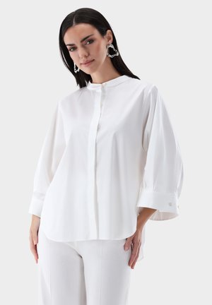 White button-up shirt with a mandarin collar, loose fit, and three-quarter sleeves. Smooth fabric and subtle buttons at the cuffs.