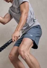 Gray athletic t-shirt with a subtle logo, paired with dark blue shorts. Both garments feature lightweight material, fitted design, and a smooth texture.