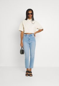 Camisa beje cropped com gola, combinada com jeans claros de cintura alta, sandálias de plataforma pretas e uma pequena bolsa preta.