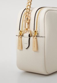 White leather rectangular handbag with gold zippers and chain strap, featuring two gold tags and a contrasting black detail on the zipper.